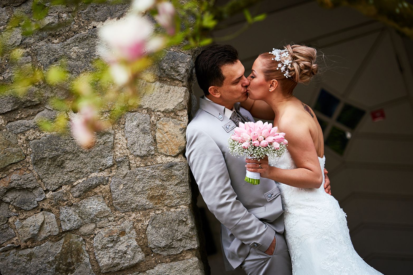 Brautpaar-Kuss an Steinmauer mit rosa Tulpen-Brautstrauß
